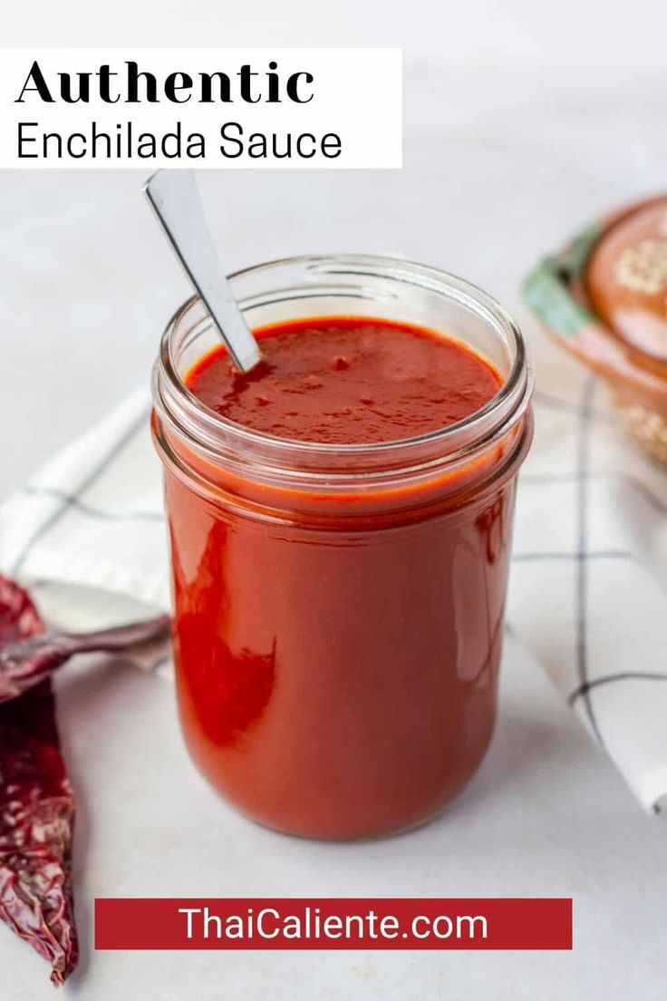 a jar filled with red sauce sitting on top of a table next to a spoon