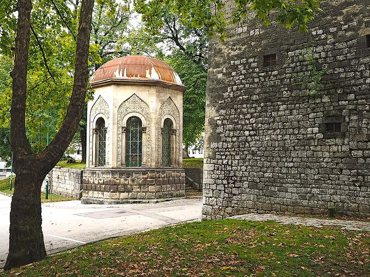 an old stone building with a rusted roof next to a brick wall and tree