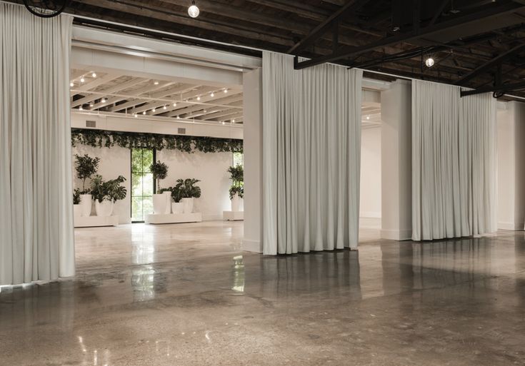 an empty room with white curtains and potted plants