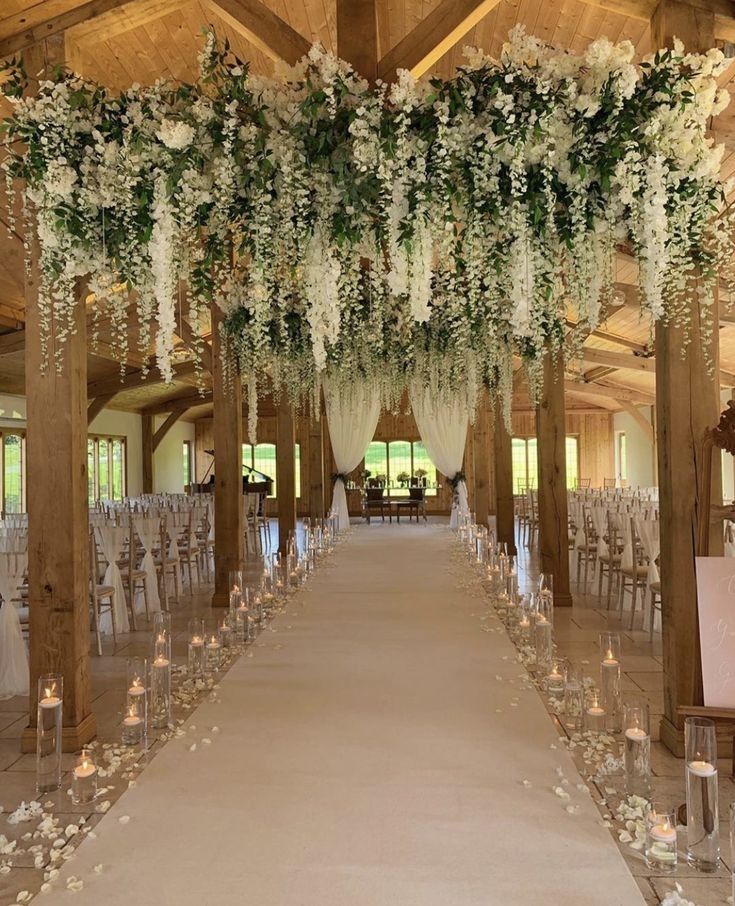 an indoor wedding venue with white flowers and greenery on the ceiling, along with candles