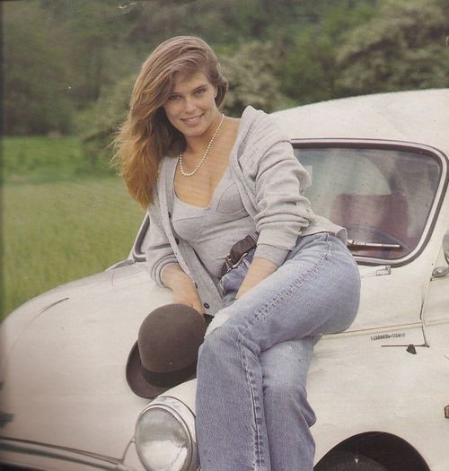 a woman sitting on the hood of a white car in front of a grassy field