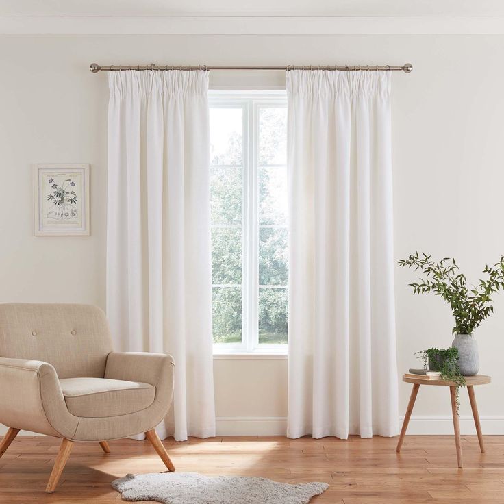 a living room with white curtains and a chair in front of a window that has a rug on the floor