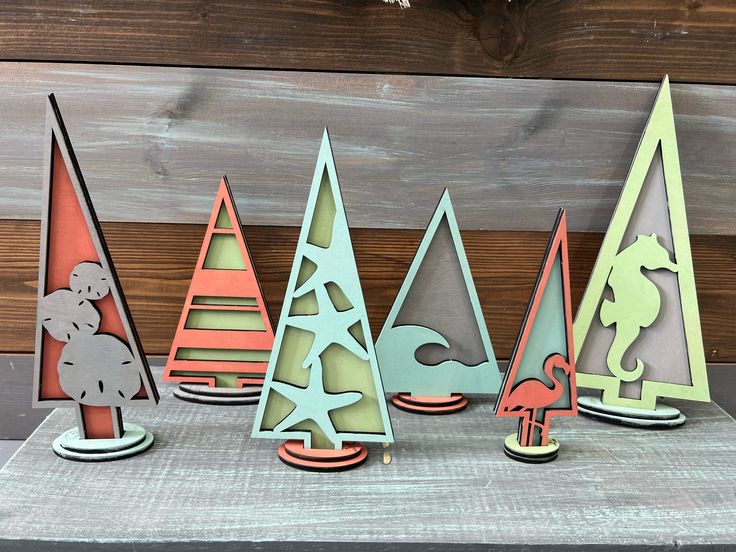 five paper christmas trees are lined up against a wooden background, each with an ornament in the shape of a horse