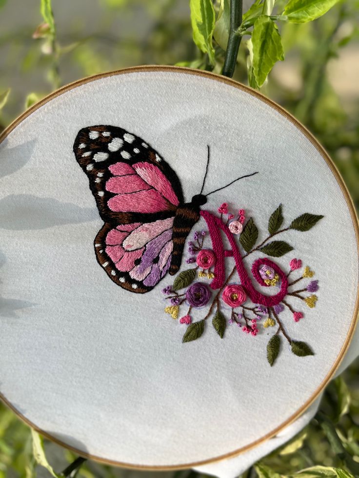 a pink and black butterfly sitting on top of a white embroideryed hoop with flowers