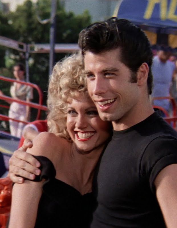 a man and woman hugging each other in front of an amusement park area with people watching