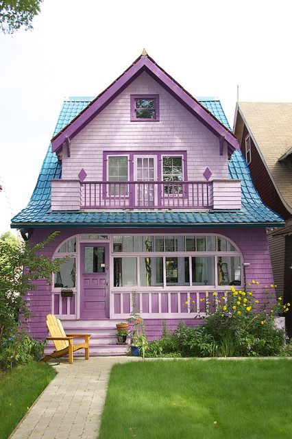 a purple house with a blue roof and green grass in the front yard, next to a yellow lawn chair