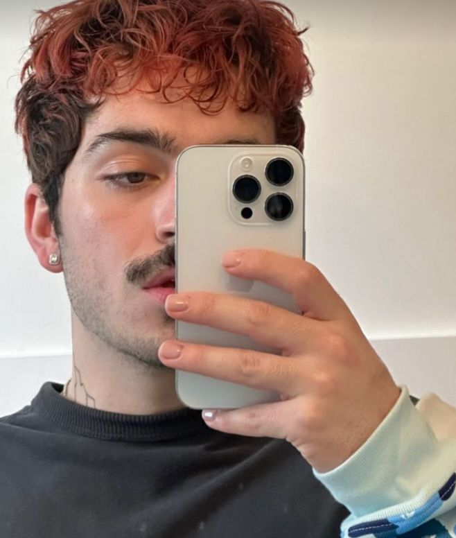 a man taking a selfie in front of his cell phone with red hair and piercings