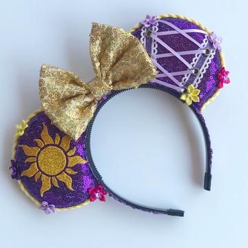 a purple and gold mouse ears headband with a sun on the side, sitting on a white surface