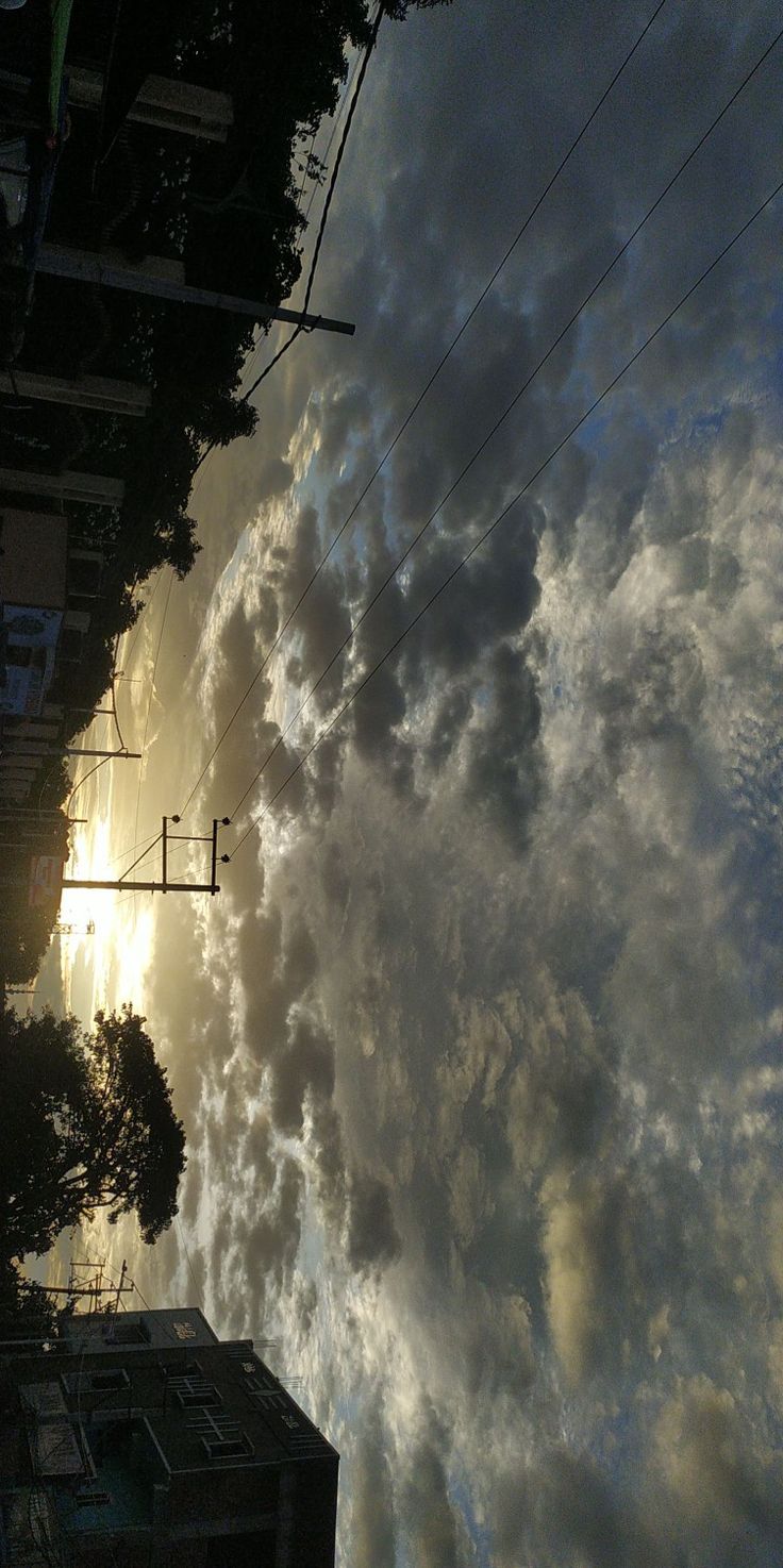 the sun is shining through clouds in the sky above some buildings and power lines on a cloudy day