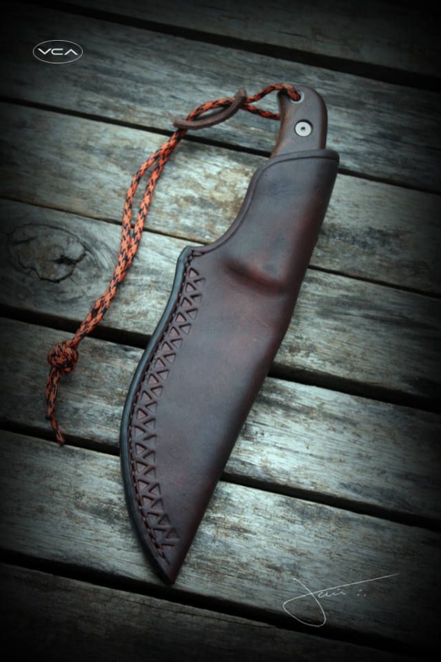 a leather sheath with an orange braid on it sitting on a wooden table next to a knife