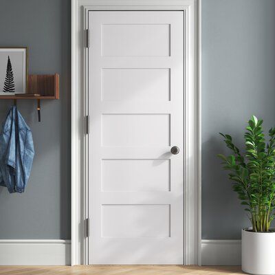 a white door in a gray room next to a potted plant and coat rack