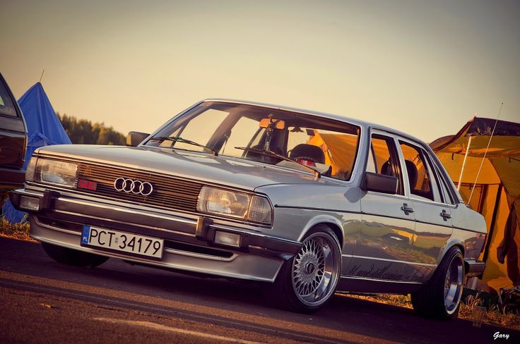 an old silver car is parked on the side of the road with tents in the background