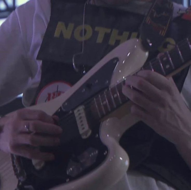 a man is playing an electric guitar in a room with other people and signs on the wall