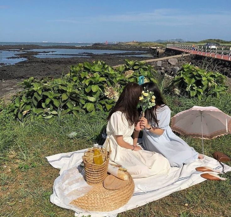 two women sitting on a blanket near the ocean