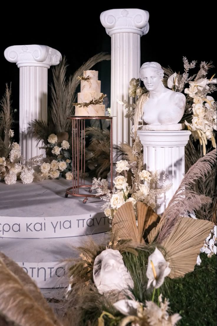 an elaborately decorated stage with white flowers and greenery on the sides, surrounded by tall pillars