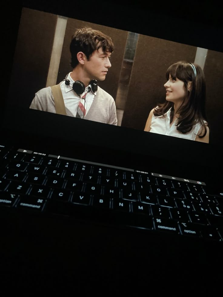 a laptop computer sitting on top of a desk with the screen showing two people talking to each other