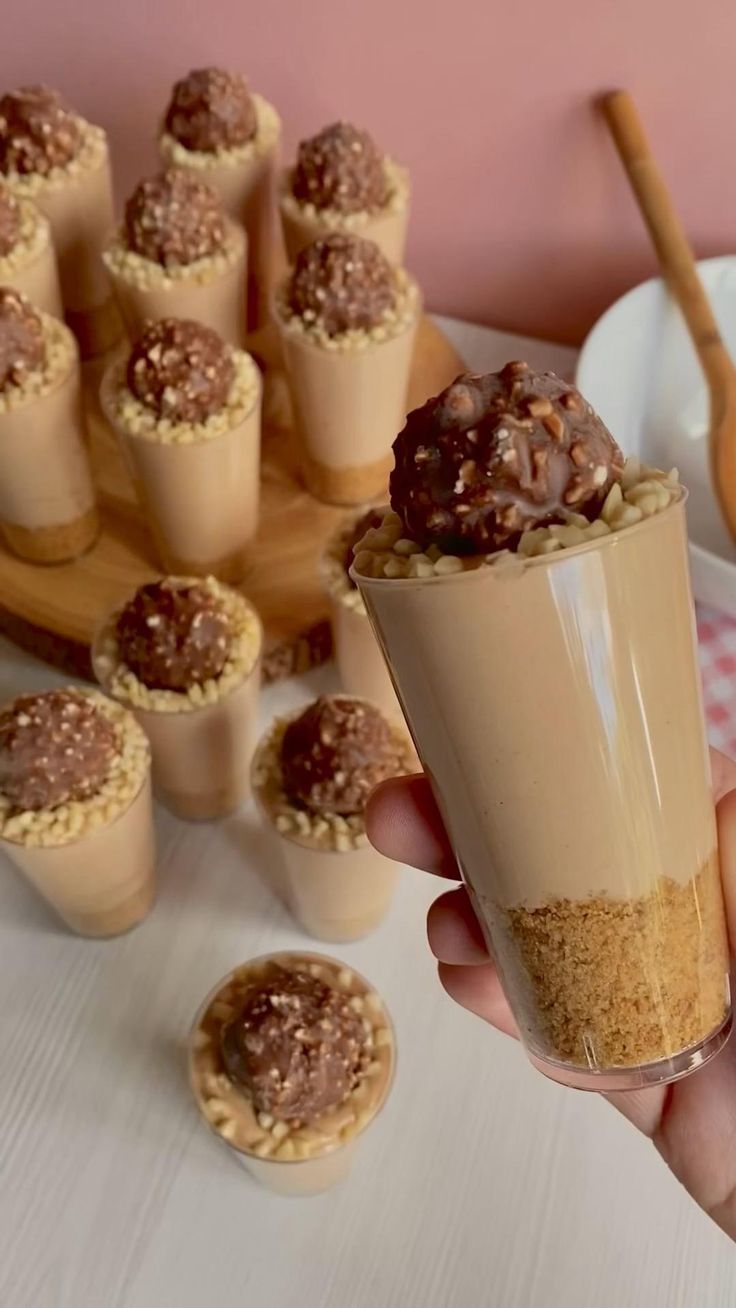 mini cheese cake in a cup being held up by someone's hand with other small desserts behind it