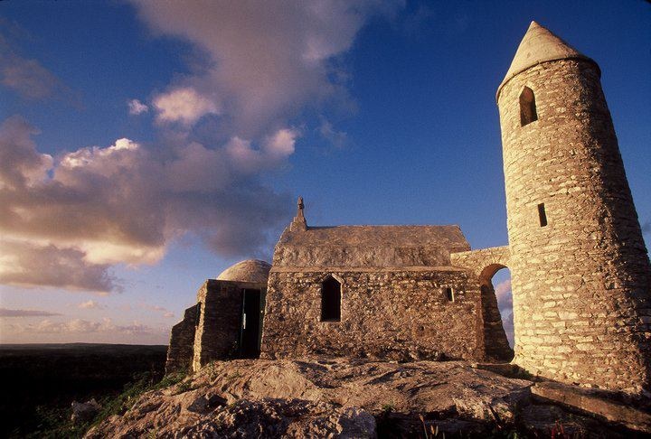 an old stone building sitting on top of a rocky hill under a cloudy blue sky