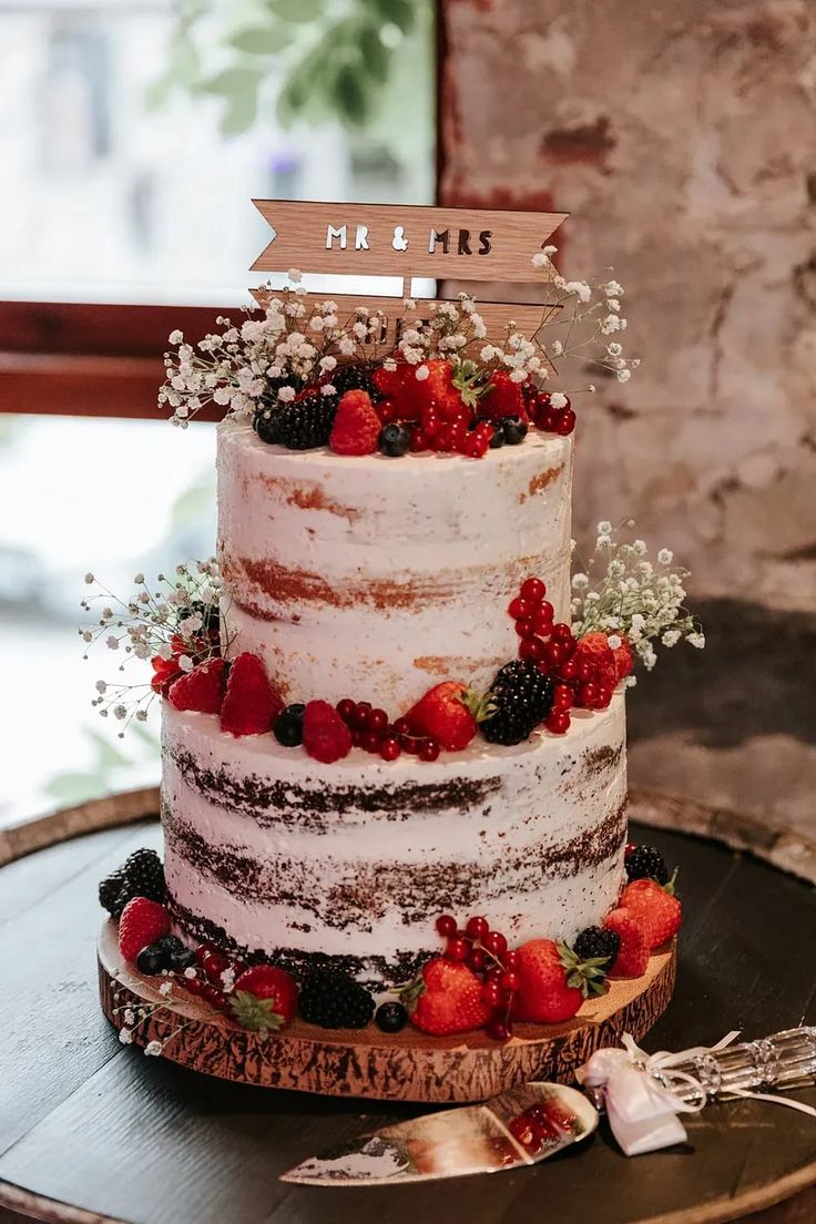 a multi layer cake with berries and flowers on it's side, sitting on top of a white table