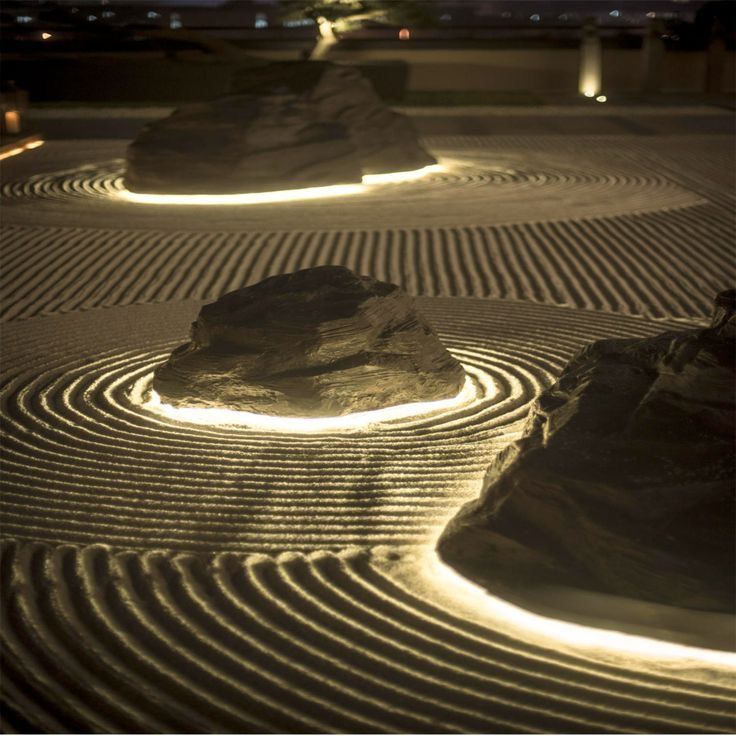 some rocks in the middle of a garden with lights on them and sand raked into circles