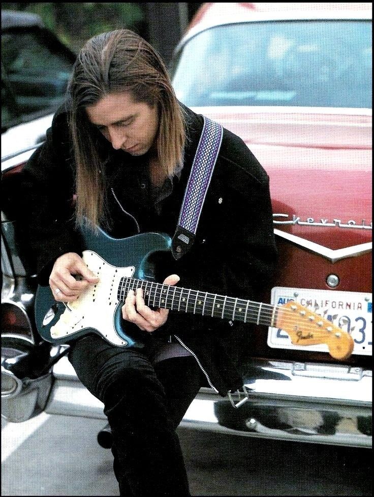 a man playing an electric guitar in front of a car