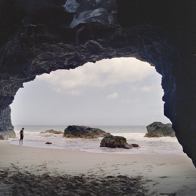 the view from inside an ocean cave looking out at the water and rocks on the beach