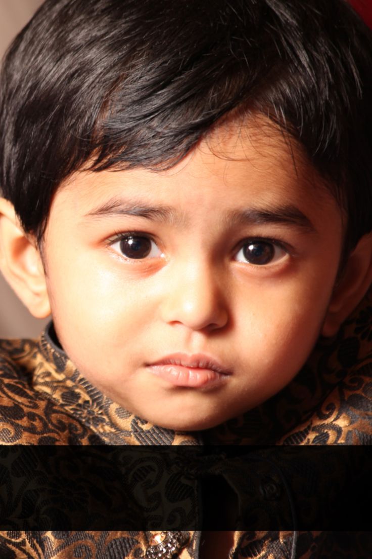 a young boy with black hair wearing a brown and gold shirt looking at the camera