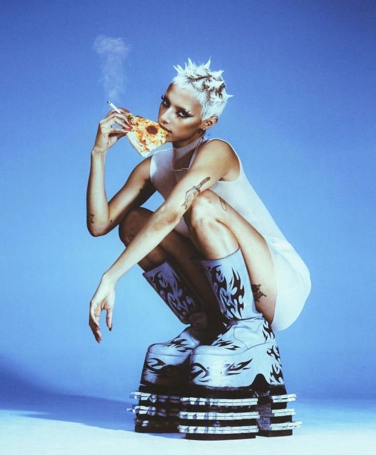 a woman sitting on top of a stack of stacked pizza boxes while holding a slice of pizza