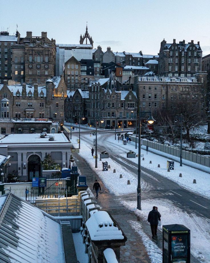 a city street is covered in snow with buildings on both sides and people walking down the sidewalk