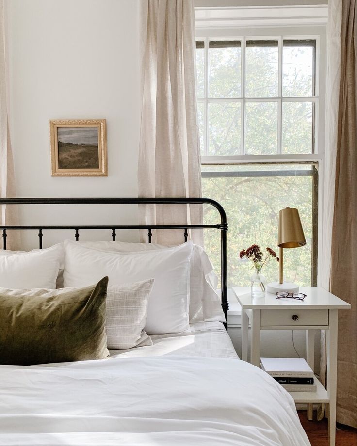 a bed with white sheets and pillows in a bedroom next to a window filled with curtains