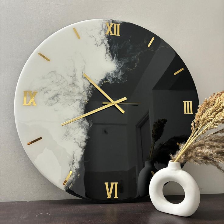 a clock that is sitting on a table next to a vase with some dried plants