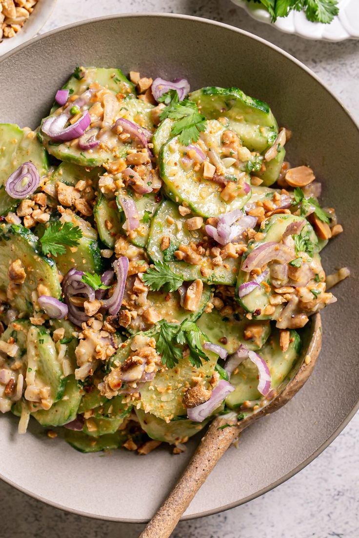 a bowl filled with cucumber salad and topped with chopped red onion, nuts