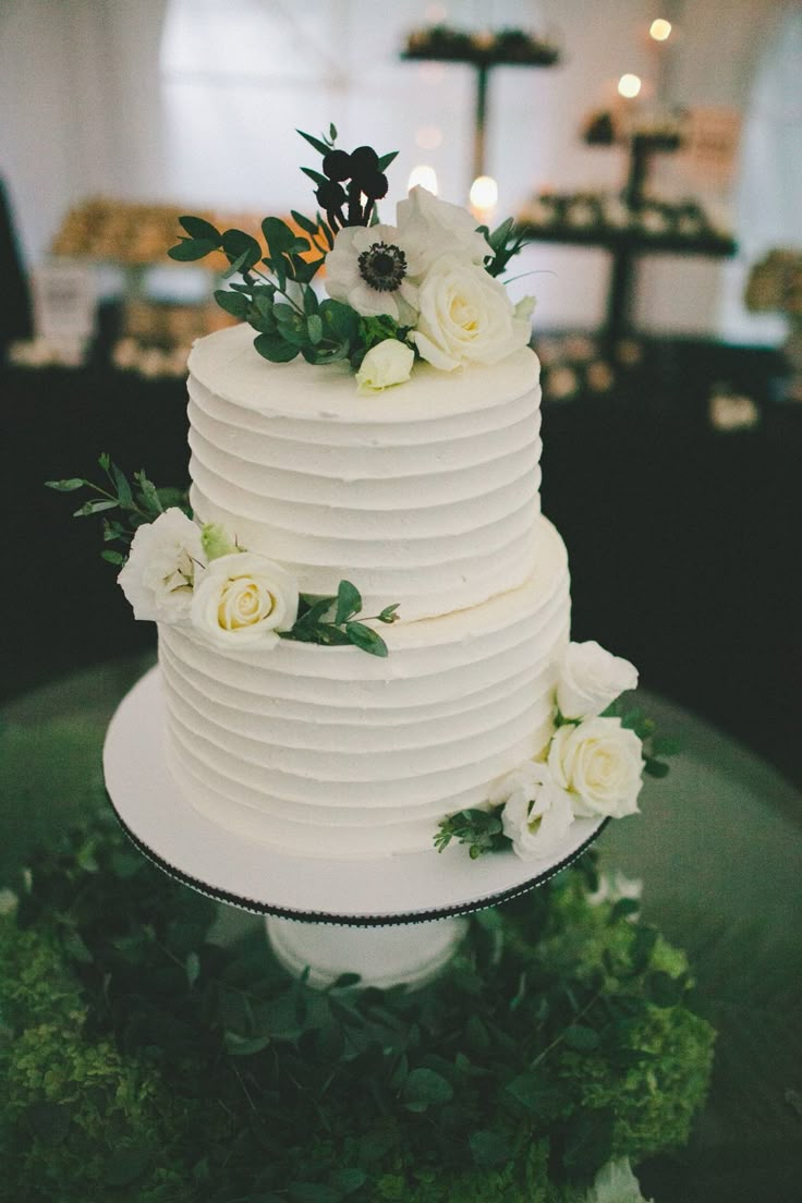 a white wedding cake sitting on top of a green table covered in flowers and greenery