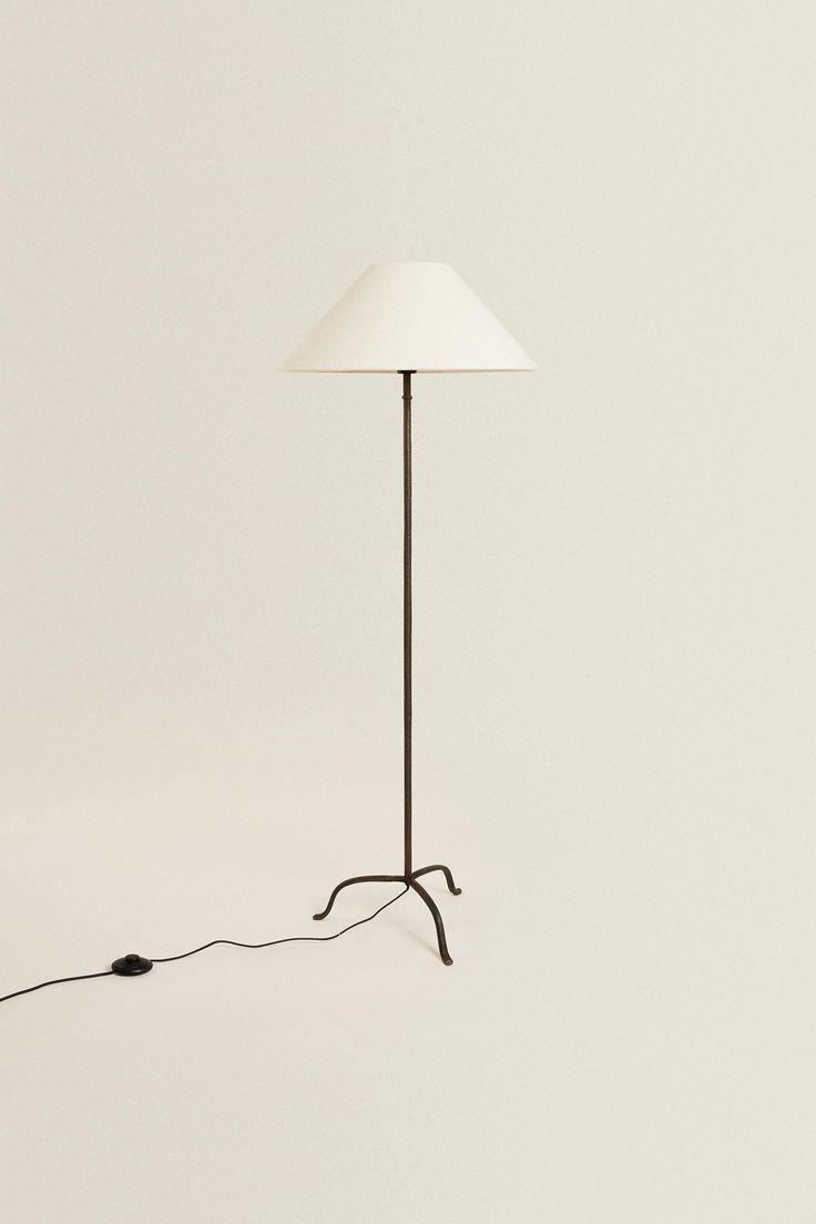 a floor lamp with a white shade on the top and a black cord attached to it