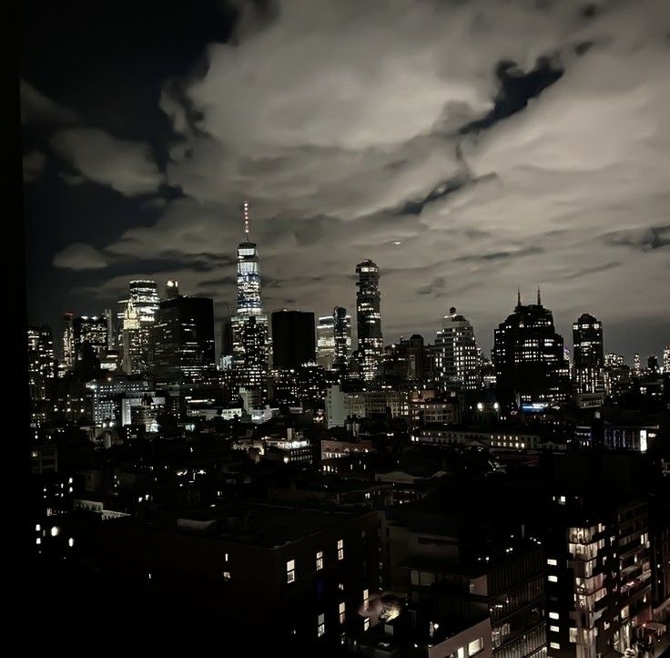 the city skyline is lit up at night, with clouds in the sky above it