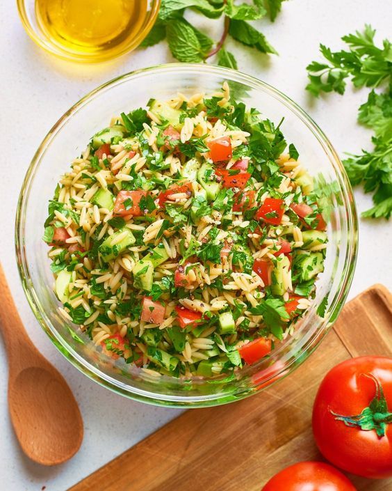 a glass bowl filled with salad next to tomatoes and parsley