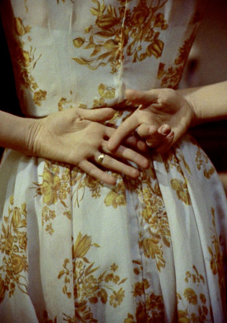 two hands holding each other while standing next to each other in front of a dress