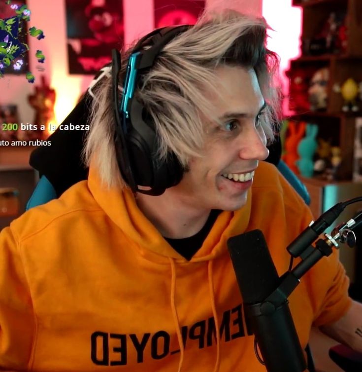 a young man wearing headphones sitting in front of a microphone and smiling at the camera