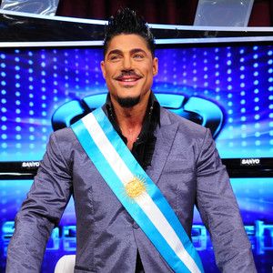 a man sitting in front of a tv wearing a blue and white sash