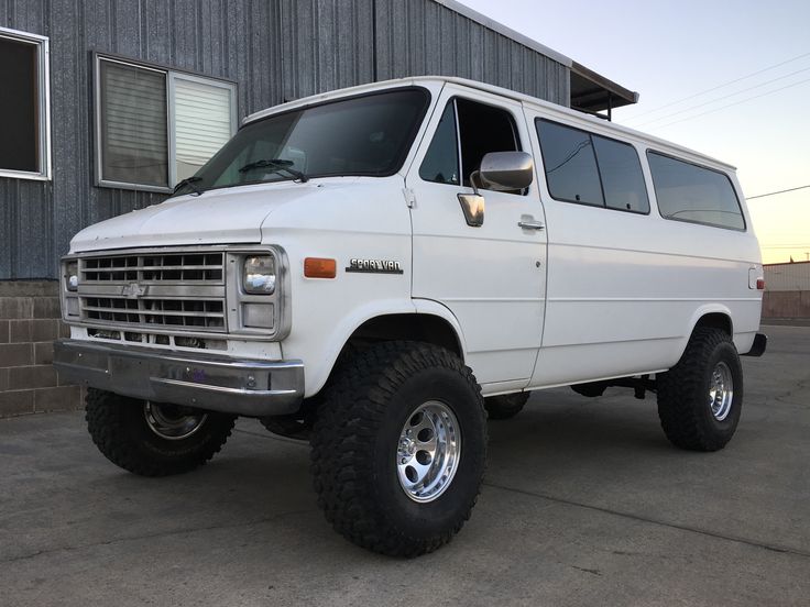 a white van parked in front of a building with large tires on it's wheels