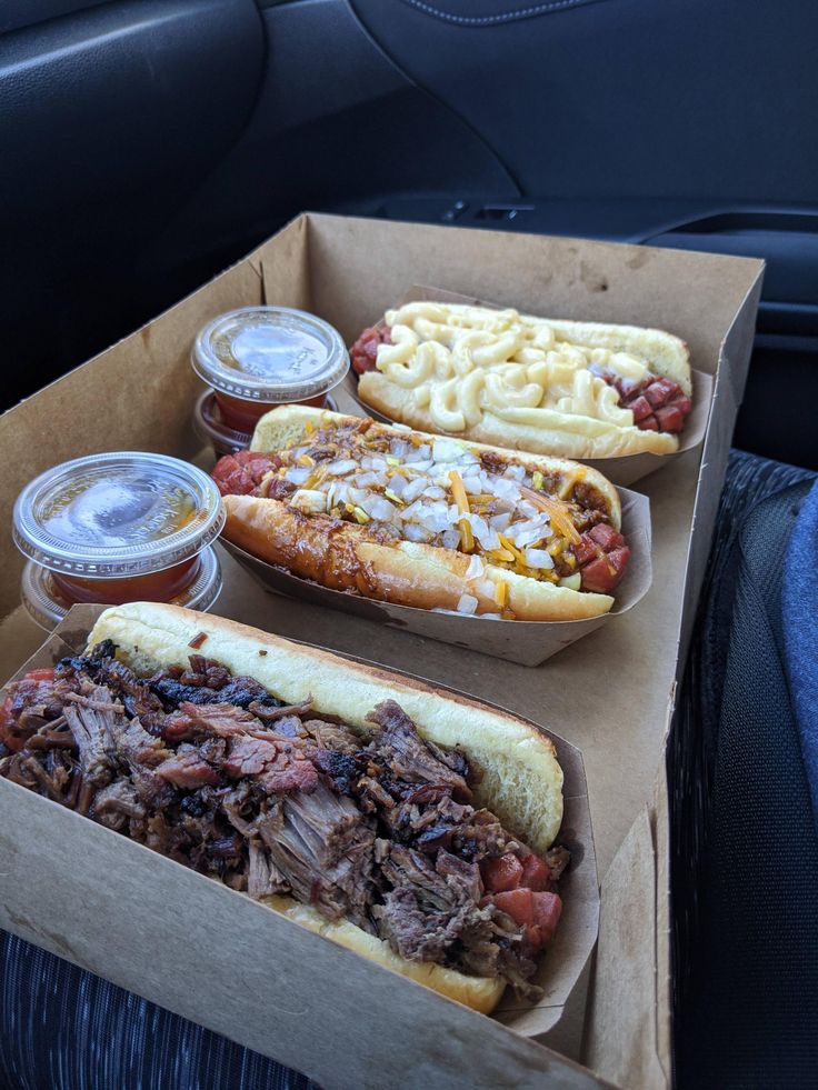 two loaded hot dogs with toppings and drinks in the back seat of a car