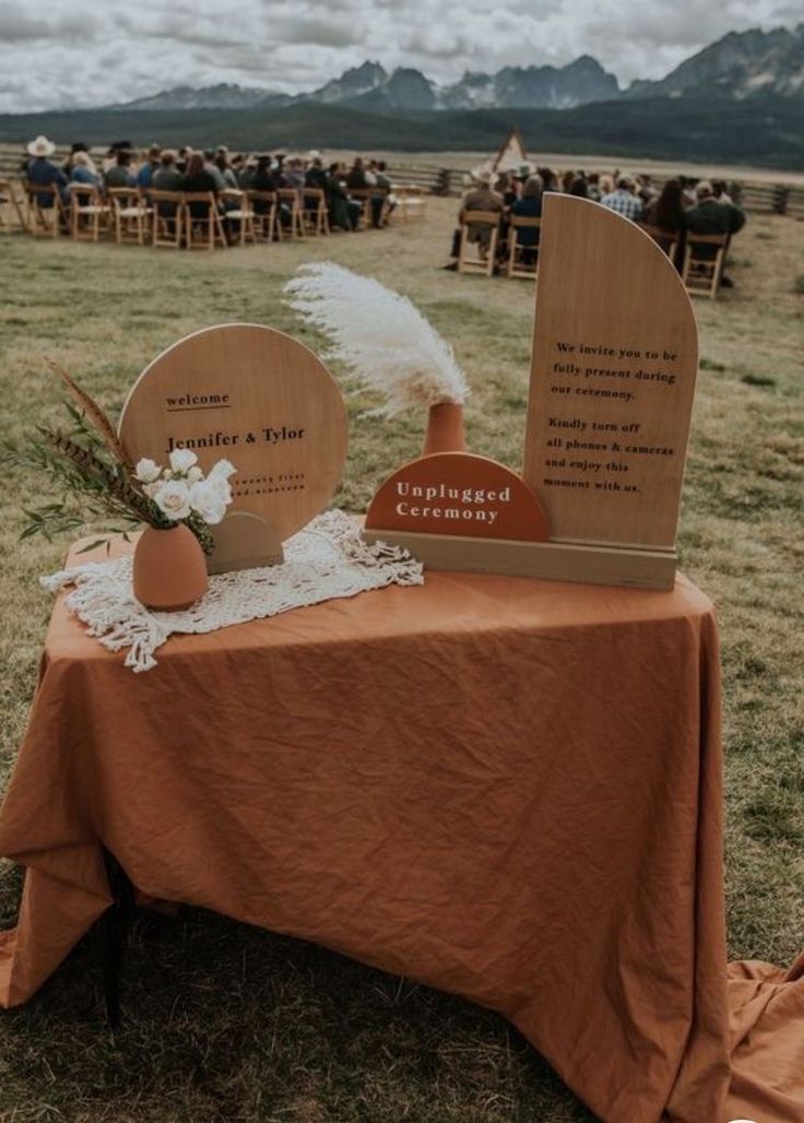 a table topped with two vases sitting on top of a grass covered field next to a wooden sign