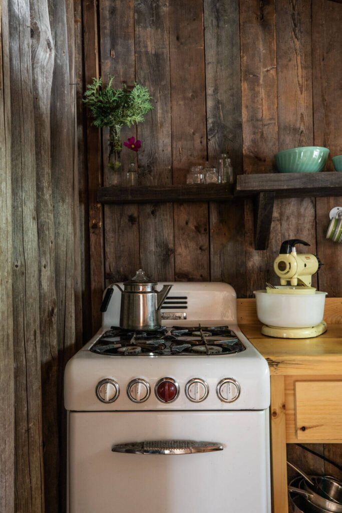 a white stove top oven sitting next to a wooden shelf filled with pots and pans