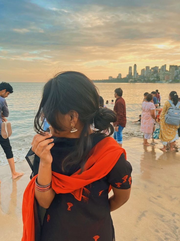 a woman standing on top of a beach next to the ocean holding a cell phone