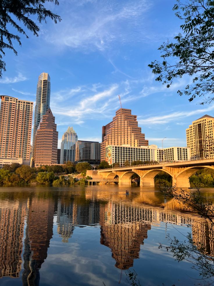 the city skyline is reflected in the still water of the river that runs through it