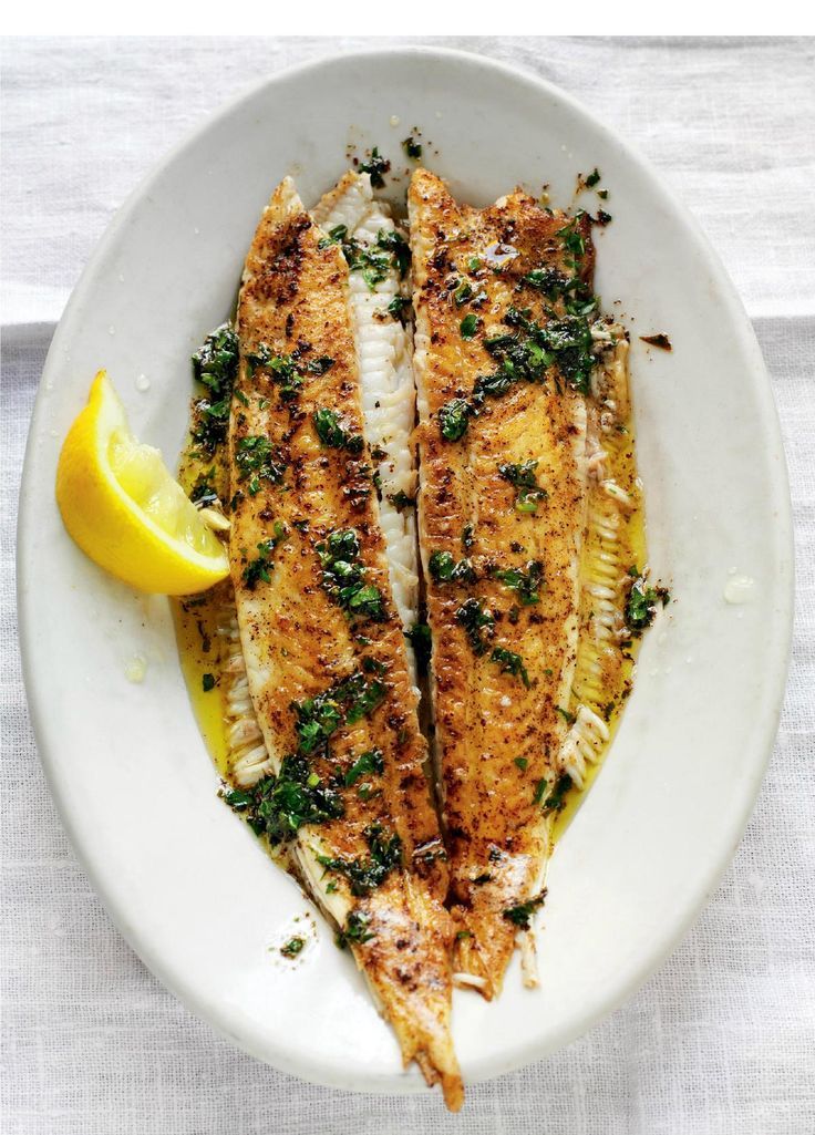 two fish fillets on a white plate with lemon wedges and parsley garnish