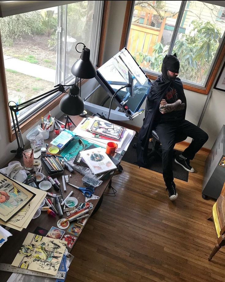 a man sitting on top of a chair next to a desk covered in clutter