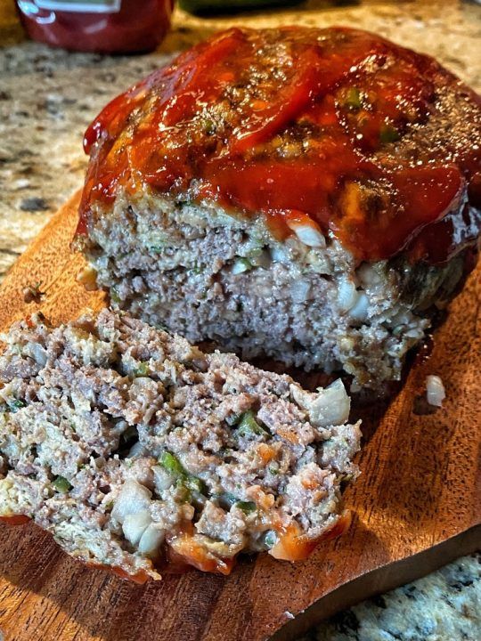 a meatloaf on a wooden cutting board with ketchup