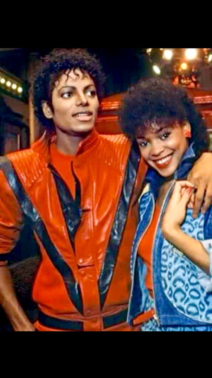 two people standing next to each other in front of a stage with lights on and one person wearing an orange jacket