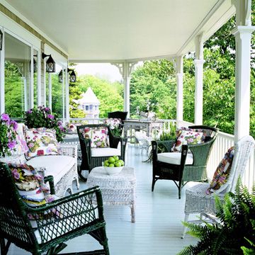 an outdoor covered porch with wicker chairs and green furniture on the front porch, surrounded by greenery